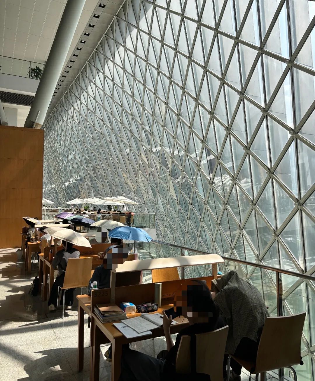 深圳图书馆玻璃不遮光，多位读者撑伞学习，回应：靠窗有一小段时间晒，可协调换位置